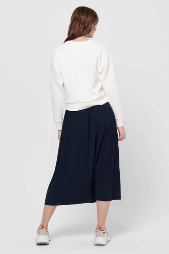 Vrouw met witte trui en blauwe plooirok, achterkant.