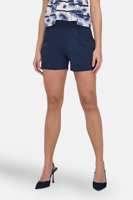 Short bleu de JDY, avec une taille haute et porté avec un haut fleuri et des baskets noires.