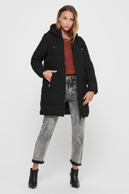 Zwarte lange jas van ONLY®, met capuchon, zakken met rits en gedragen met een bruine trui, grijze jeans en zwarte laarzen.
