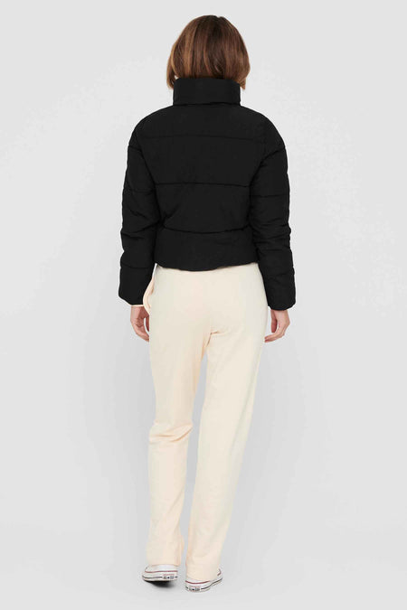 Manteau court noir d'ONLY, avec un col haut et porté avec des pantalons crème et des baskets blanches.