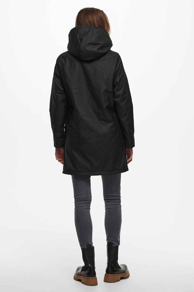 Zwarte regenjas van ONLY, gezien van achteren, met een capuchon, gecombineerd met een grijze jeans en zwarte laarzen.
