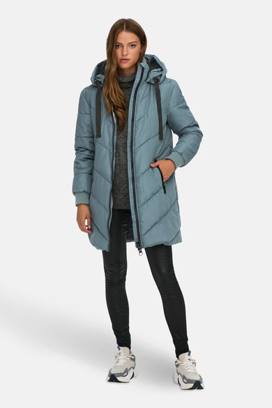 Manteau long bleu de JDY, avec des coutures diagonales et un capuchon, associé à une chemise grise et une legging noire.