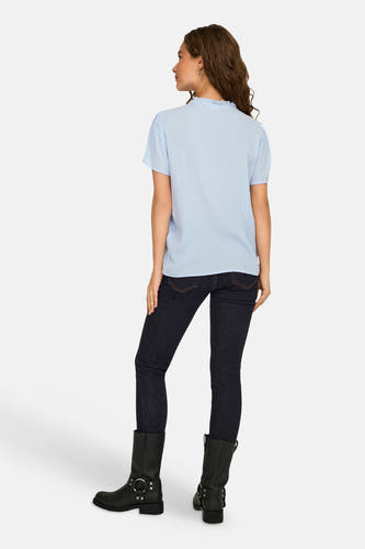 Chemisier bleu à manches courtes de JDY avec un motif à pois subtil et un col à volants, porté sur un jean foncé et des bottes noires.