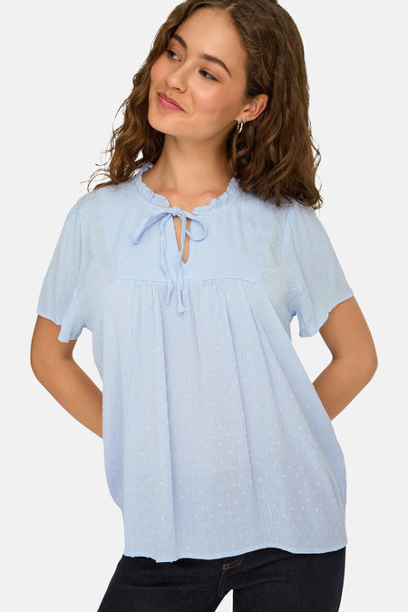 Chemisier bleu clair à manches courtes de JDY, avec tissu texturé, pois subtils, col à volants et détail de nœud.