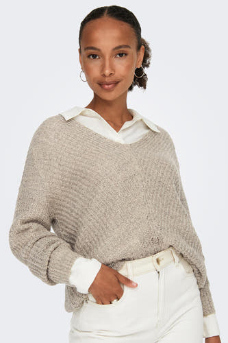 Pull à col V en cuir de JDY, porté avec une chemise blanche et un pantalon blanc avec ceinture.