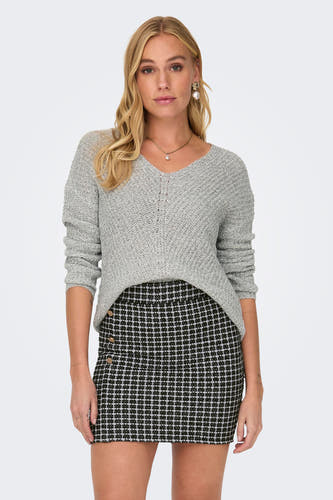 Pull blanc à col V de JDY, associé à une mini-jupe rayée et des bijoux dorés.