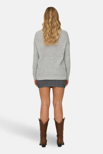 Pull-over blanc à col V de JDY, porté avec une mini-jupe rayée et des bottes de cow-boy brunes.