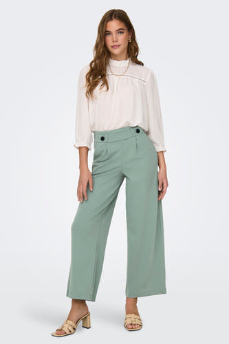 Pantalon de costume vert de JDY, avec des jambes larges et porté avec une blouse blanche et un collier doré.