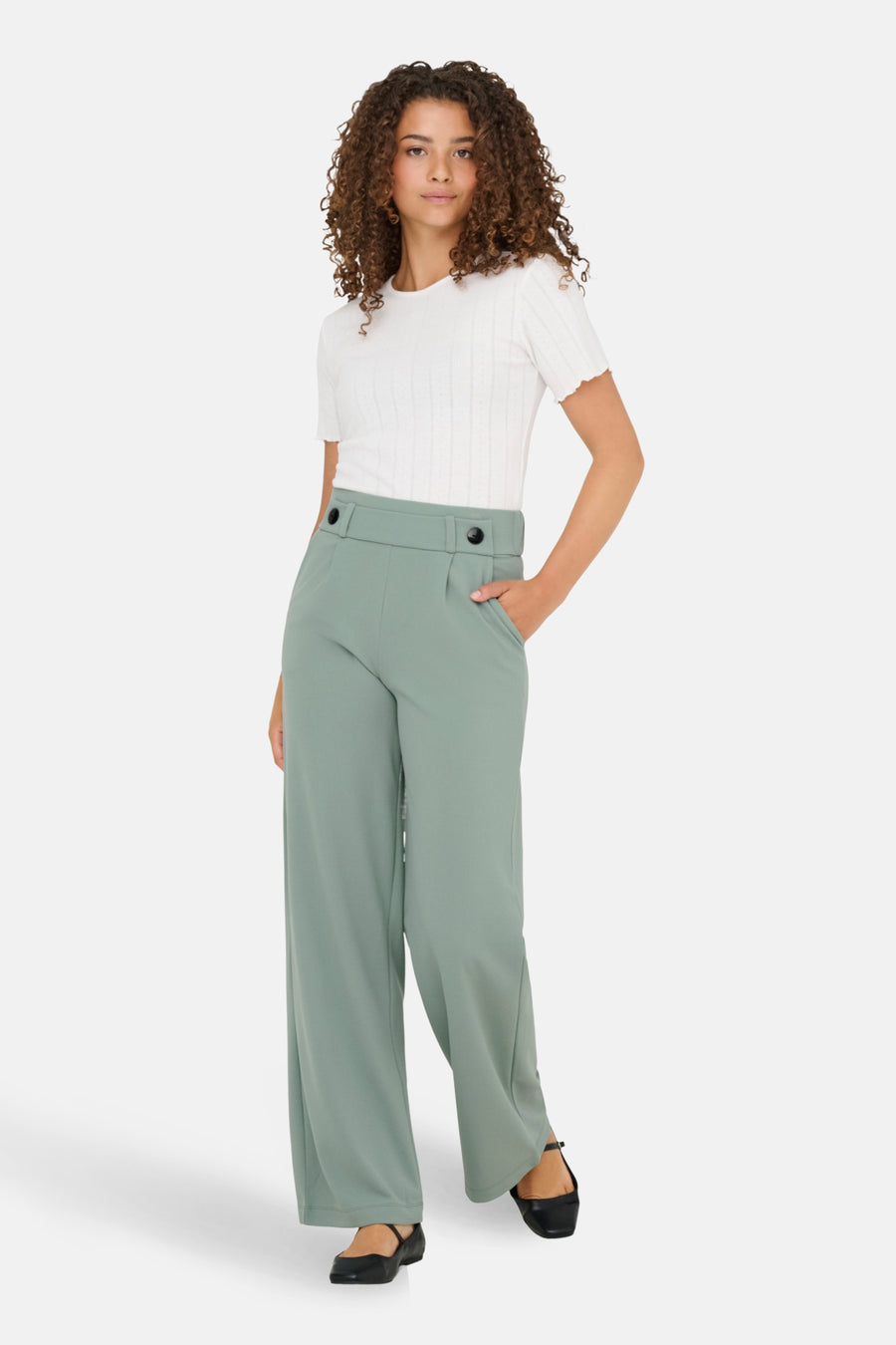Vrouw in witte top en groene wijde pantalon.