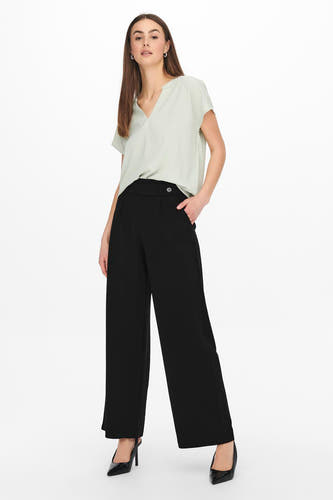 Pantalon de costume noir JDY, avec une taille haute et des jambes larges, associé à une chemise verte claire et à des escarpins noirs.