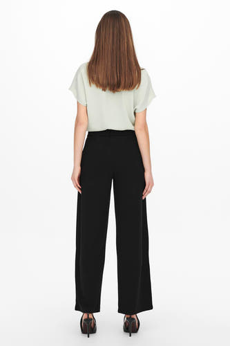 Pantalon de costume noir JDY, vu de l'arrière avec une blouse verte claire et des talons hauts.