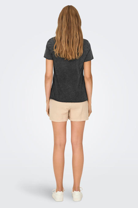 T-shirt noir à manches courtes d'ONLY, vu de derrière, avec des shorts en coton beige décontractés et des chaussures blanches.