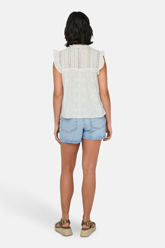 Vrouw van achteren in een witte top, blauwe spijkerbroek, en groene sandalen.