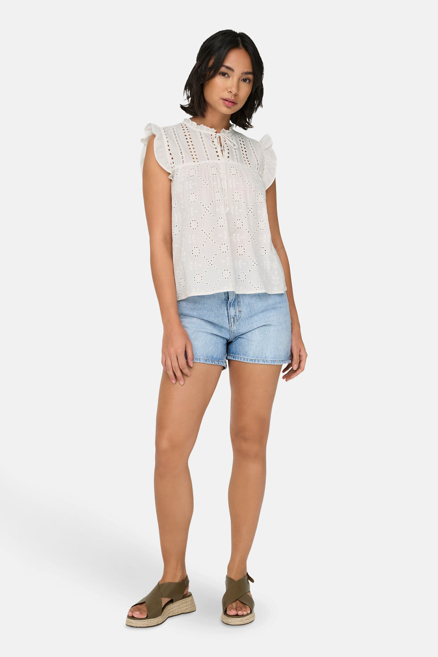 Vrouw met witte blouse, blauwe spijkerbroek en groene sandalen.