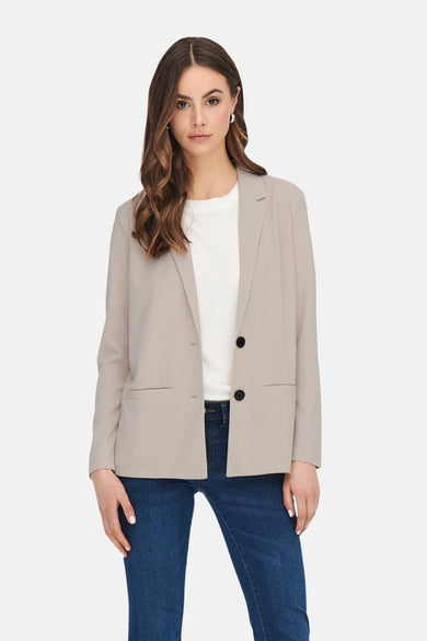 Blazer beige de JDY, avec des manches longues et des boutons noirs, porté sur un T-shirt blanc et un jeans foncé.