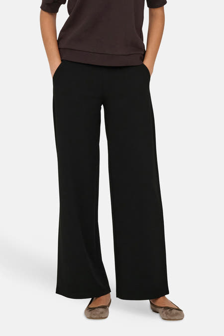 Pantalon de costume noir de JDY à jambes larges, porté par un mannequin avec les mains dans les poches et des ballerines marron.