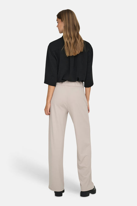 Pantalon de costume gris de JDY à jambes larges et taille élastique, porté par un mannequin avec un chemisier noir et des chaussures épaisses, vue arrière.