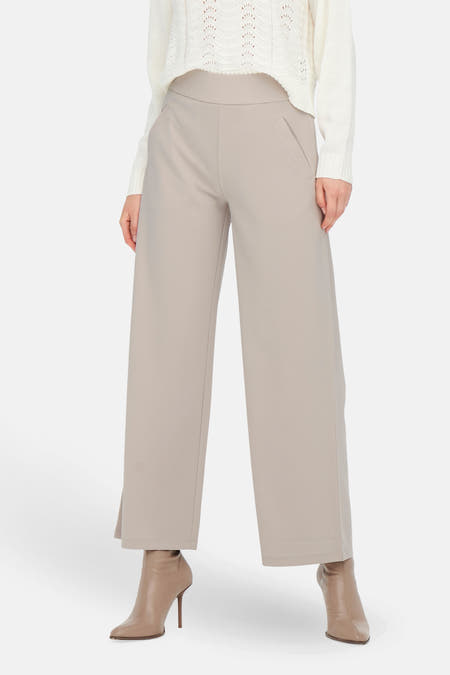 Pantalon gris de costume JDY, avec une main dans la poche et un pull tricoté blanc.
