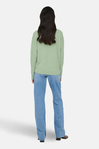 Vrouw in groene trui en blauwe jeans, van achteren gezien.