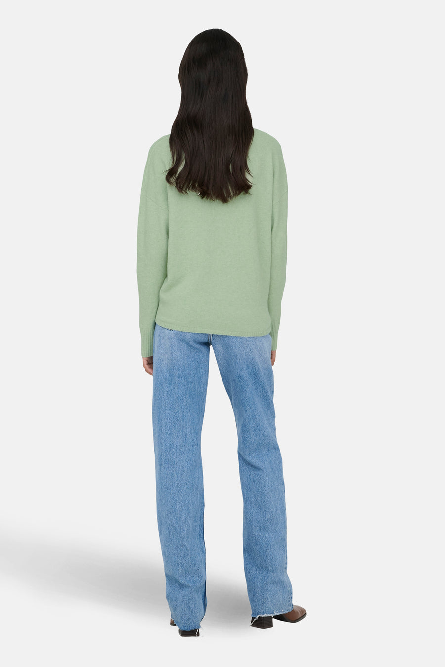 Vrouw in groene trui en blauwe jeans, van achteren gezien.