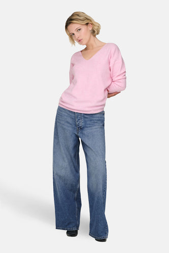 Vrouw met roze trui en wijde jeans op witte achtergrond.