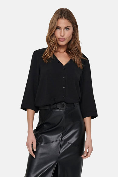 Blouse noire de JDY, avec col V et manches trois-quarts, associée à une jupe en cuir avec fente et bottes.
