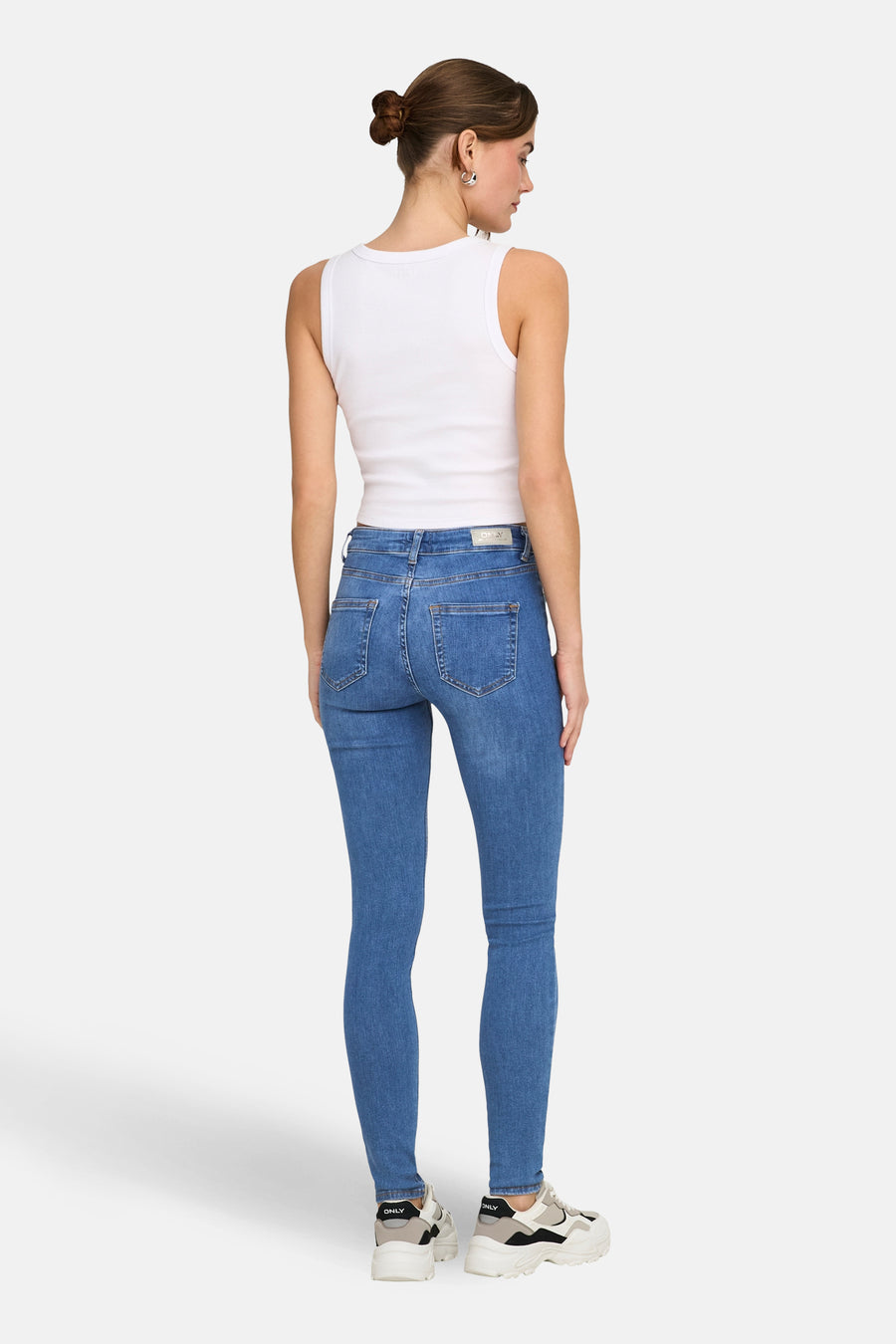 Blauwe skinny jeans van ONLY, met hoge taille en achterkant van het model in een wit hemd en chunky sneakers.
