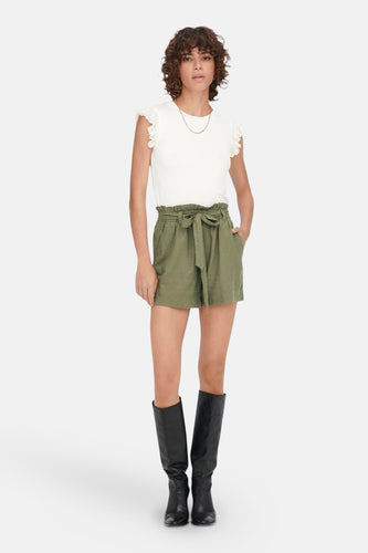 Vrouw in witte top, groene shorts en zwarte laarzen.