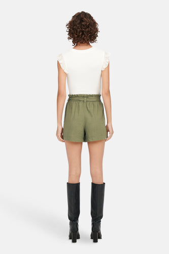 Model van achteren, witte top, groene shorts, zwarte laarzen.
