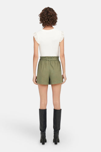 Achterkant van een vrouw in een witte top met groene shorts en zwarte laarzen.