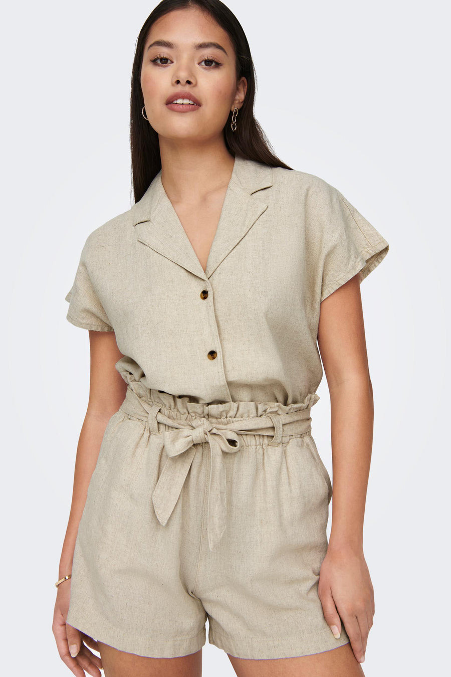 Vrouw in beige linnen blouse en shorts met riem.