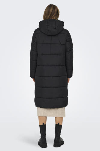 Zwarte lange jas van ONLY, met een capuchon, gedragen over een beige jurk en zwarte laarzen.