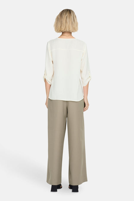 Witte blouse met driekwartmouwen van JDY, gezien van achteren, met lange groene broek en gouden ketting.