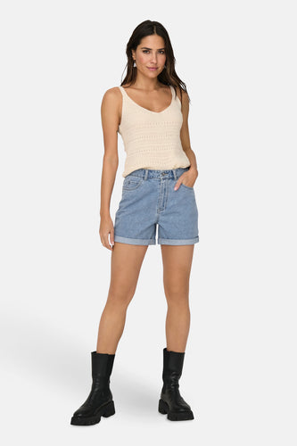 Vrouw in gehaakte top, denim shorts en zwarte laarzen.