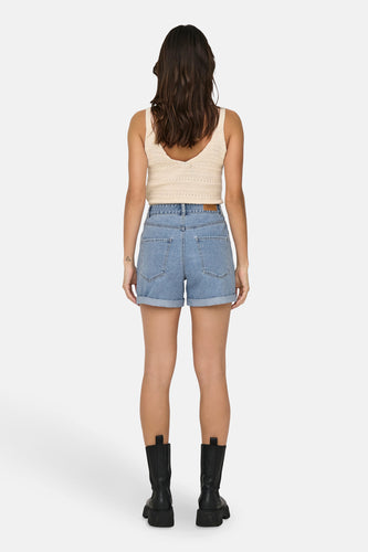 Achterkant van een vrouw in denimshorts en een gebreide top, met zwarte laarzen tegen een witte achtergrond.