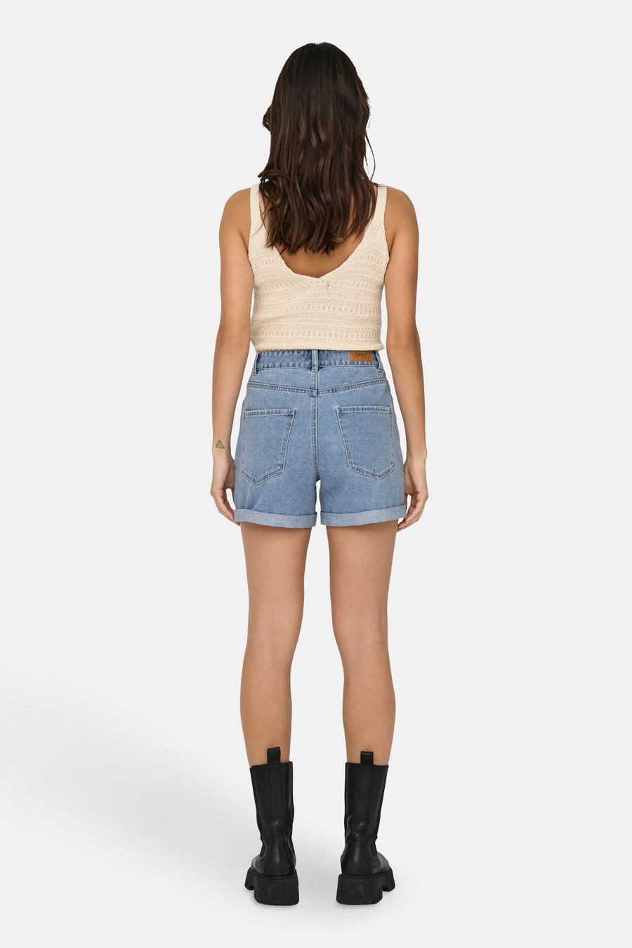 Achterkant van een vrouw in denimshorts en een gebreide top, met zwarte laarzen tegen een witte achtergrond.