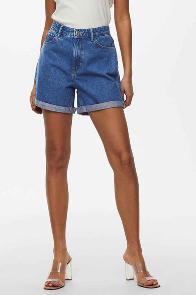 Short en denim bleu ONLY, avec des poches rabattues et porté avec un haut blanc et des sandales transparentes.