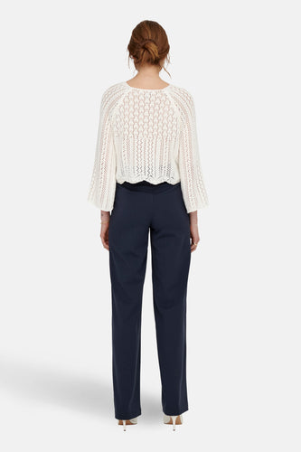 Achterkant van een vrouw in een gebreide trui en donkerblauwe broek, met witte hakken.