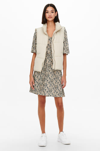 Gilet écru de JDY, porté sur une robe à imprimé paisley et des baskets blanches.