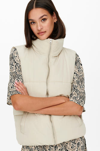Gilet écru JDY avec col montant et fermeture éclair, porté sur une blouse à imprimé paisley.