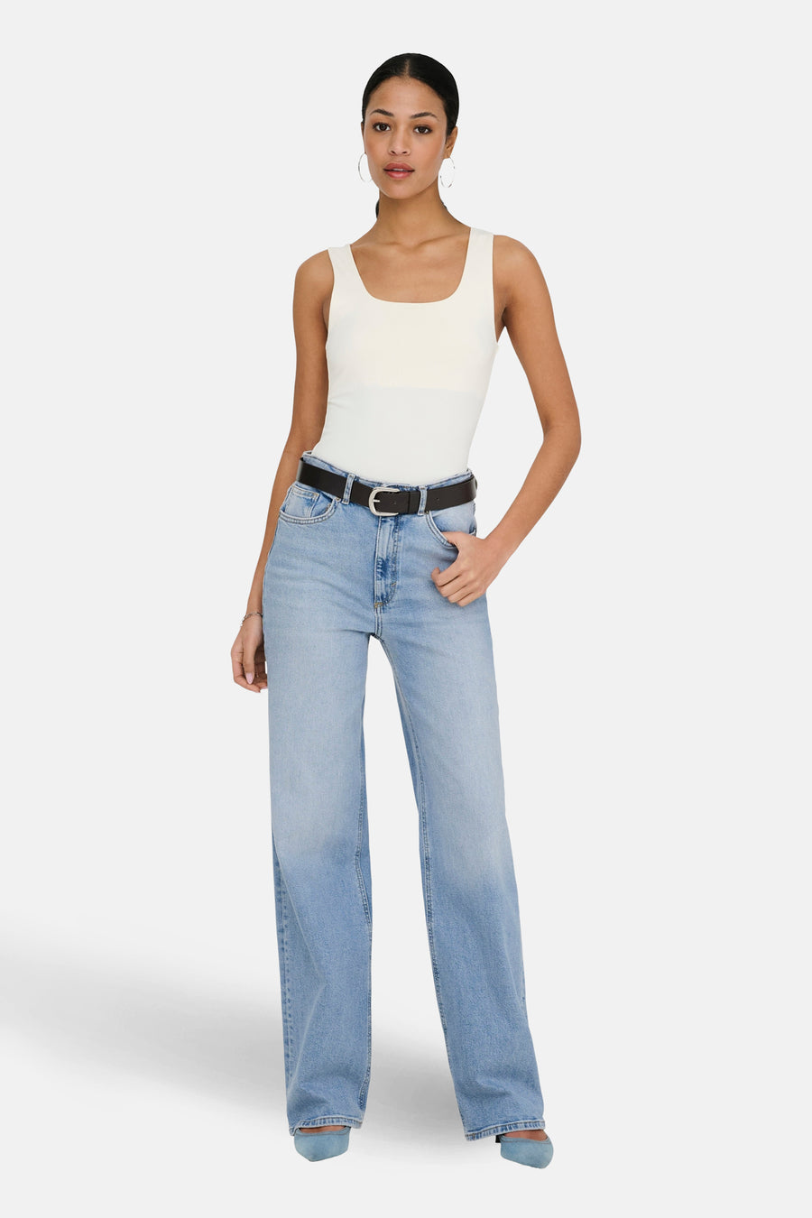 Lichtblauwe wijde jeans van ONLY, gedragen met een zwarte riem, witte tanktop en lichtblauwe schoenen.