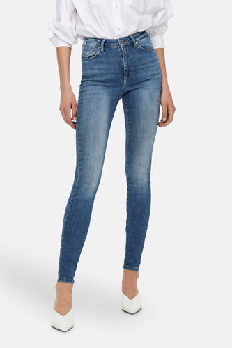 Jean skinny bleu ONLY, avec un lavage classique et associé à une blouse blanche.