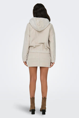 Gilet écru ONLY, avec un capuchon et une texture corduroy, porté avec une mini-jupe coordonnée et des bottes brunes.