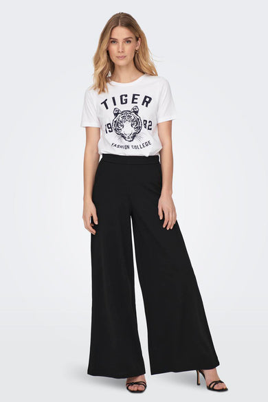 Pantalon noir de JDY, avec des jambes larges et porté avec un T-shirt blanc à imprimé tigre et des baskets noires.