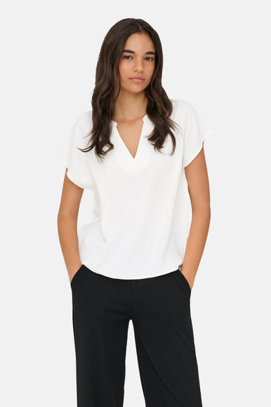 Chemisier blanc de JDY avec col en V, manches courtes amples et tissu texturé, porté avec un pantalon noir.