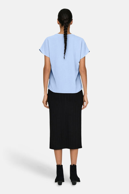 Chemisier bleu à manches courtes de JDY, avec une texture tissée et combiné avec une jupe noire et des bottines.