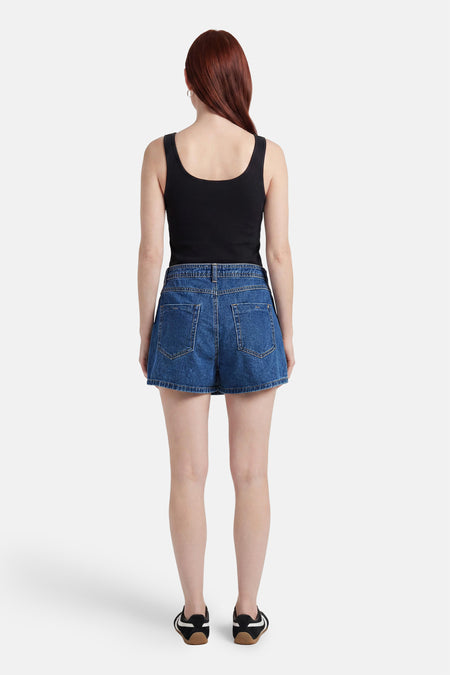 Donkerblauwe denim skort van ONLY® met twee achterzakken, gezien van achteren, gedragen met zwarte top en sneakers.