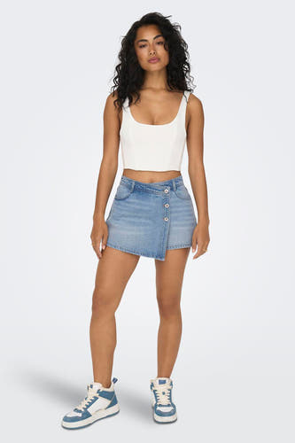 Short de denim bleu clair ONLY, avec une fermeture à bouton asymétrique et porté avec un haut blanc et des baskets hautes.