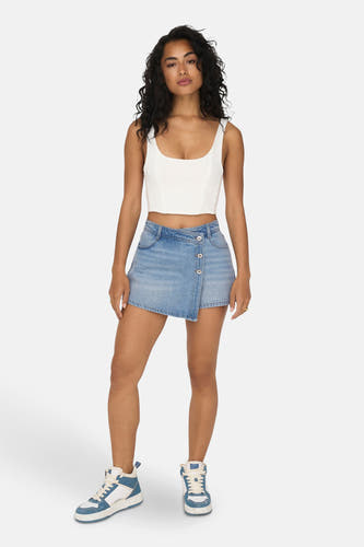Short de denim bleu clair ONLY®, avec une fermeture à bouton asymétrique, associé à une chemise blanche et des baskets bleues et blanches.