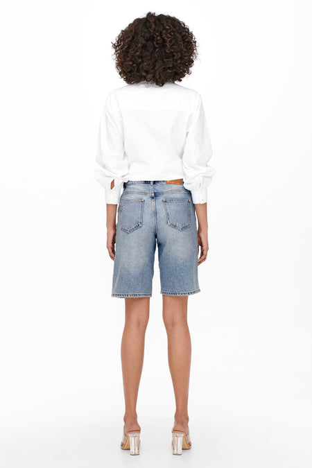 Short en denim bleu clair de ONLY, avec un dos nu, associé à une chemise blanche et des talons transparents.